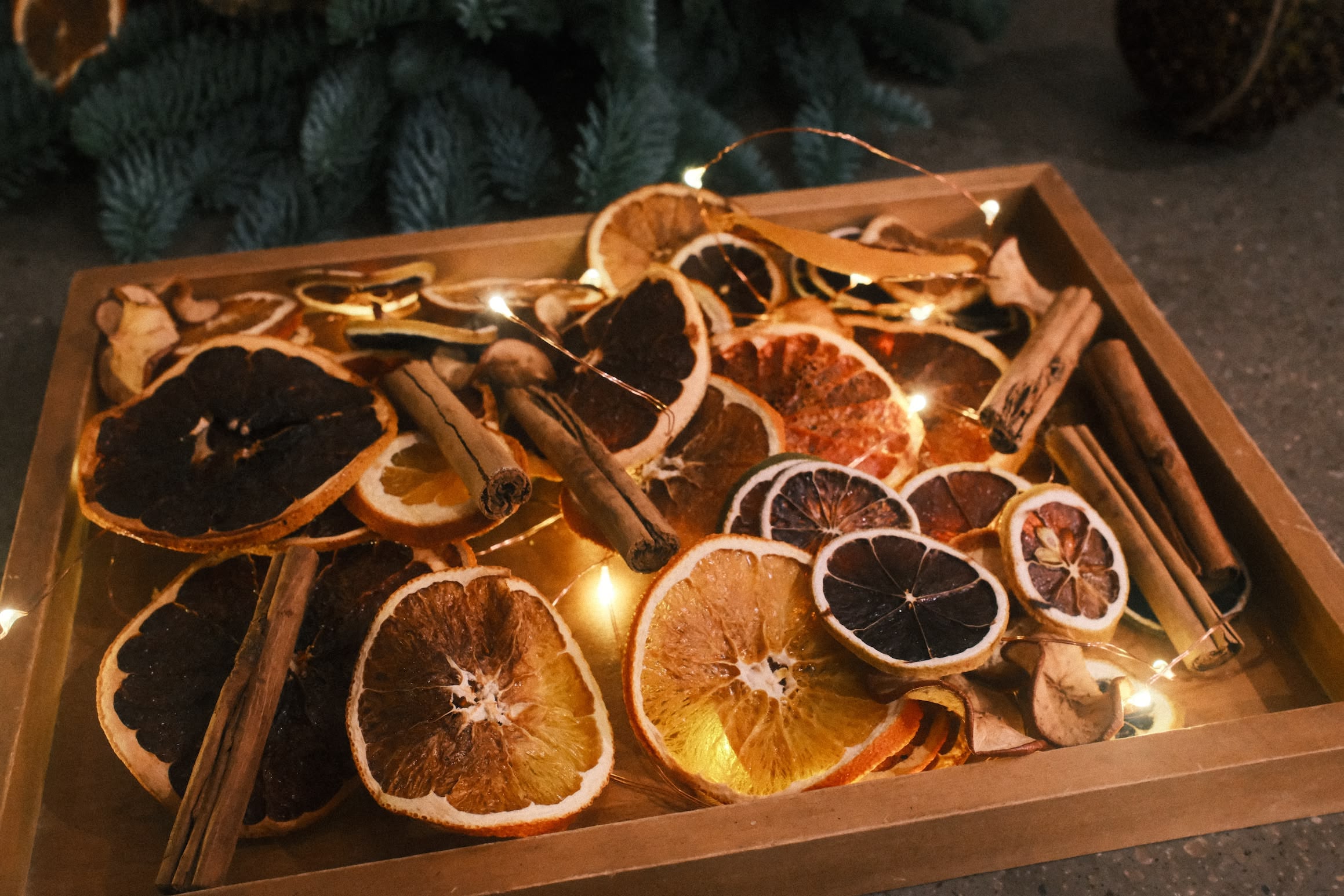 A wooden tray containing dried citrus fruit and cinamon bark and a few fairy lights