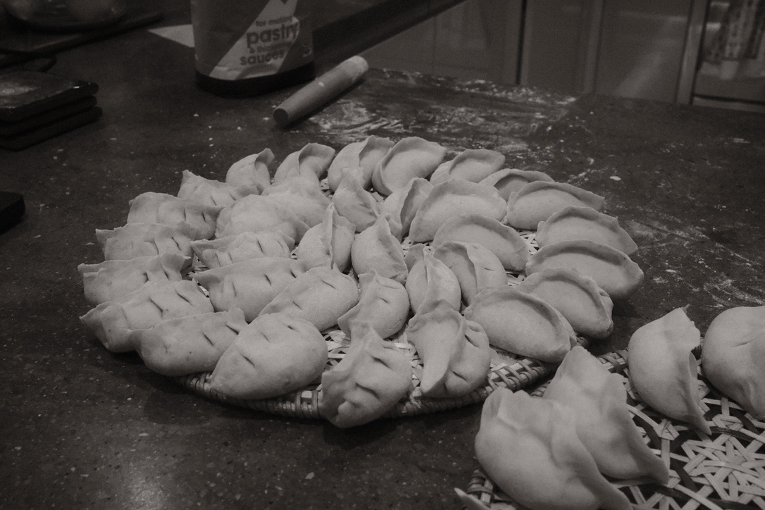 a black and white photo showing a tray full of uncooked dumplings on a flour covered work surface
