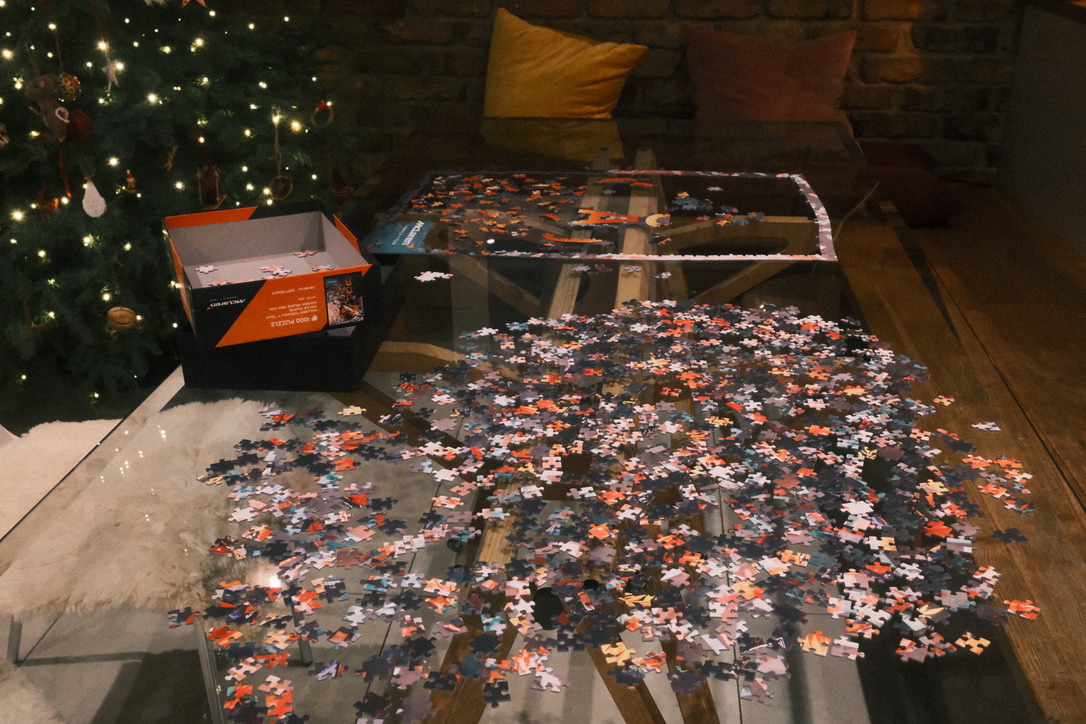 an un-finished puzzle on a glass table, christmas tree in the background