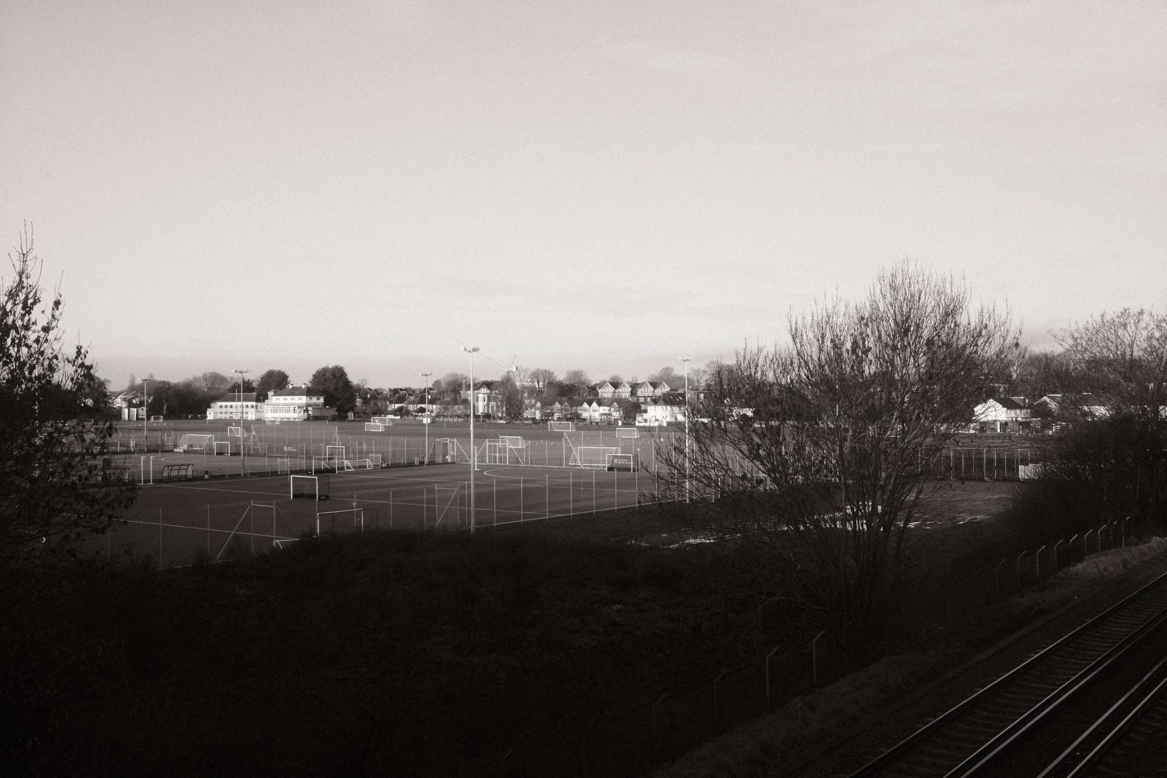 a black and white photo of playing fields, a railway track in the foreground