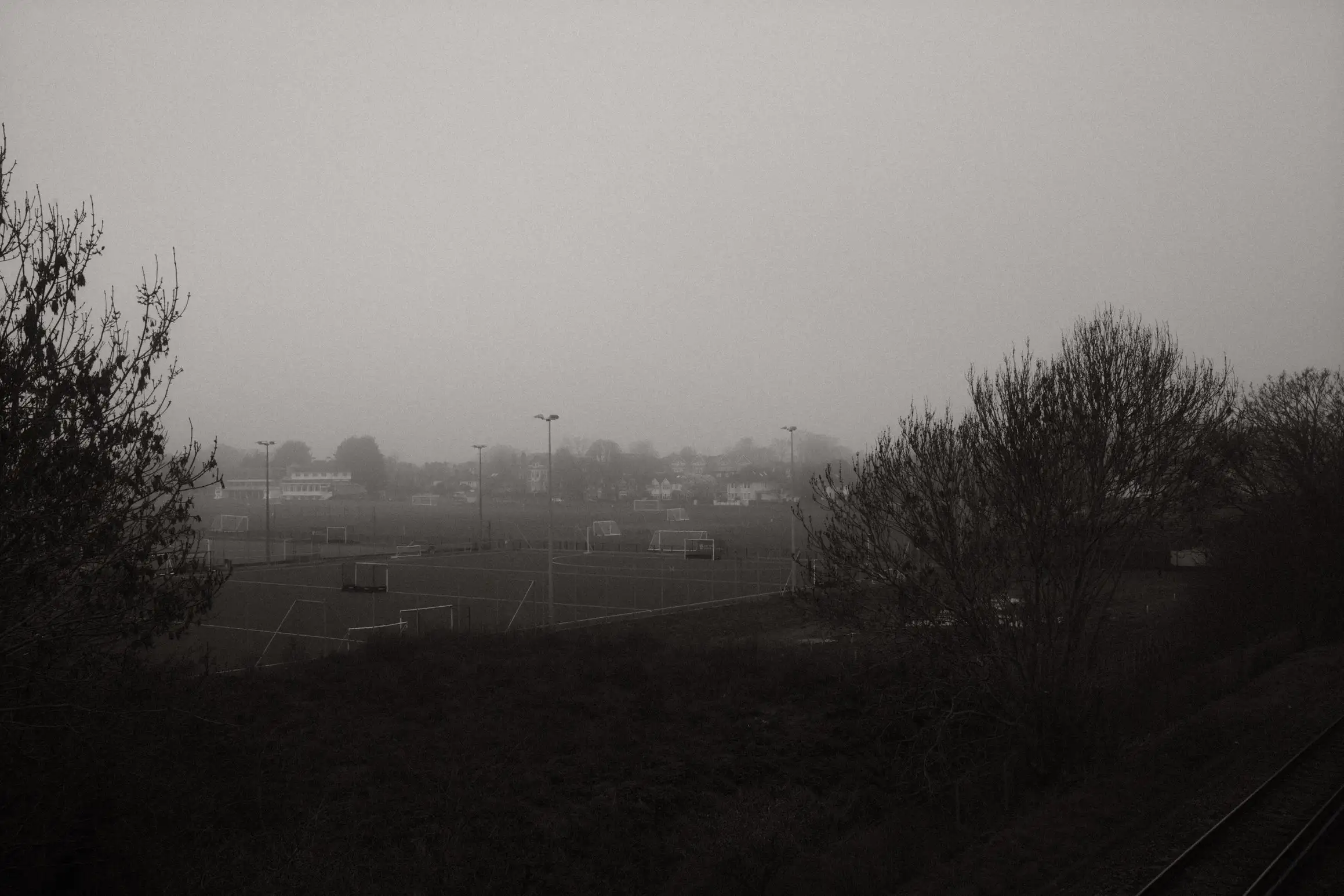 A black and white photo looking out over playing fields on a foggy morning.