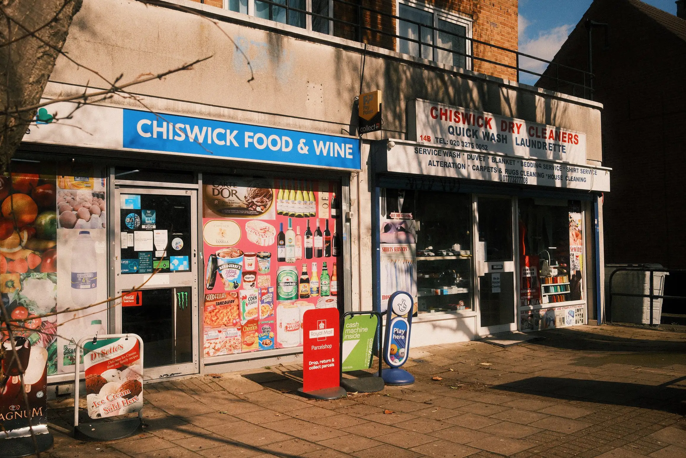a photo of two adjacent shops, Chiswick Food & Wine and Chiswick Dry Cleaners, the front of each covered with posters and advertisements